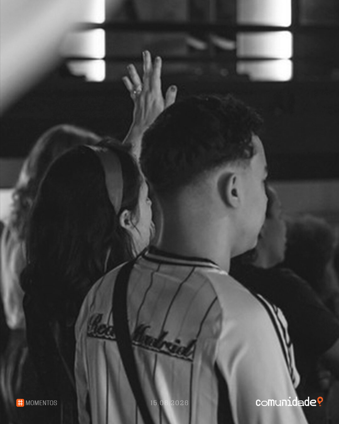Em preto e branco, jovens de costas com as mãos erguidas durante o louvor